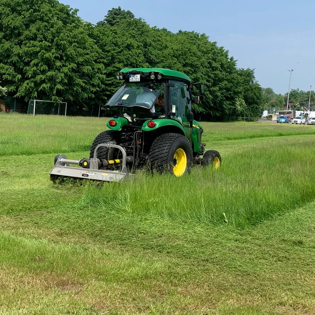 John-Deere-Traktor mit Mähwerk beim Mähen einer größeren Grünfläche.