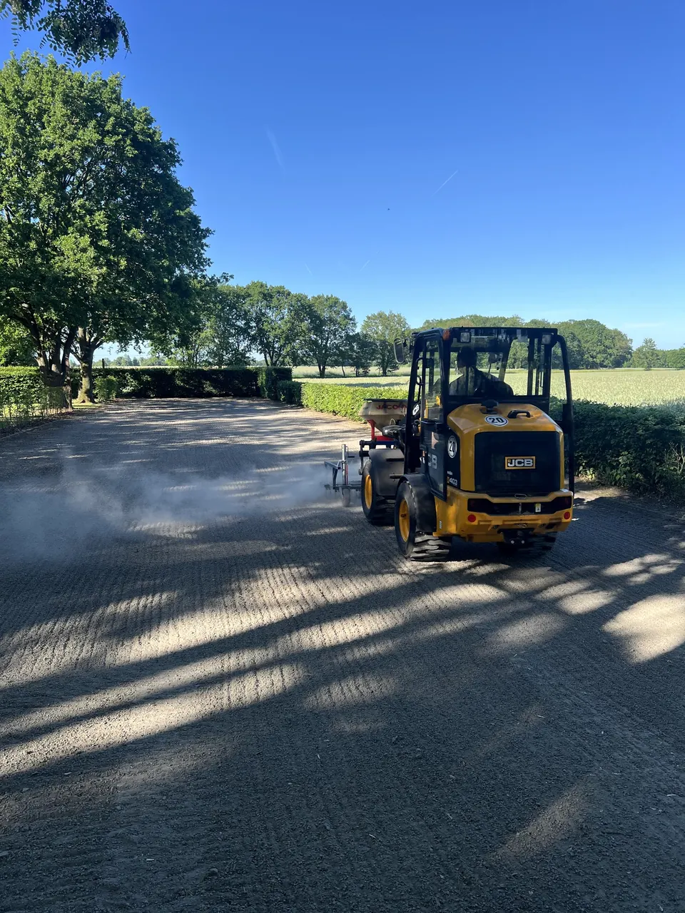 Kompakte Arbeitsmaschine auf einer befestigten Wegefläche neben einer Grünanlage.