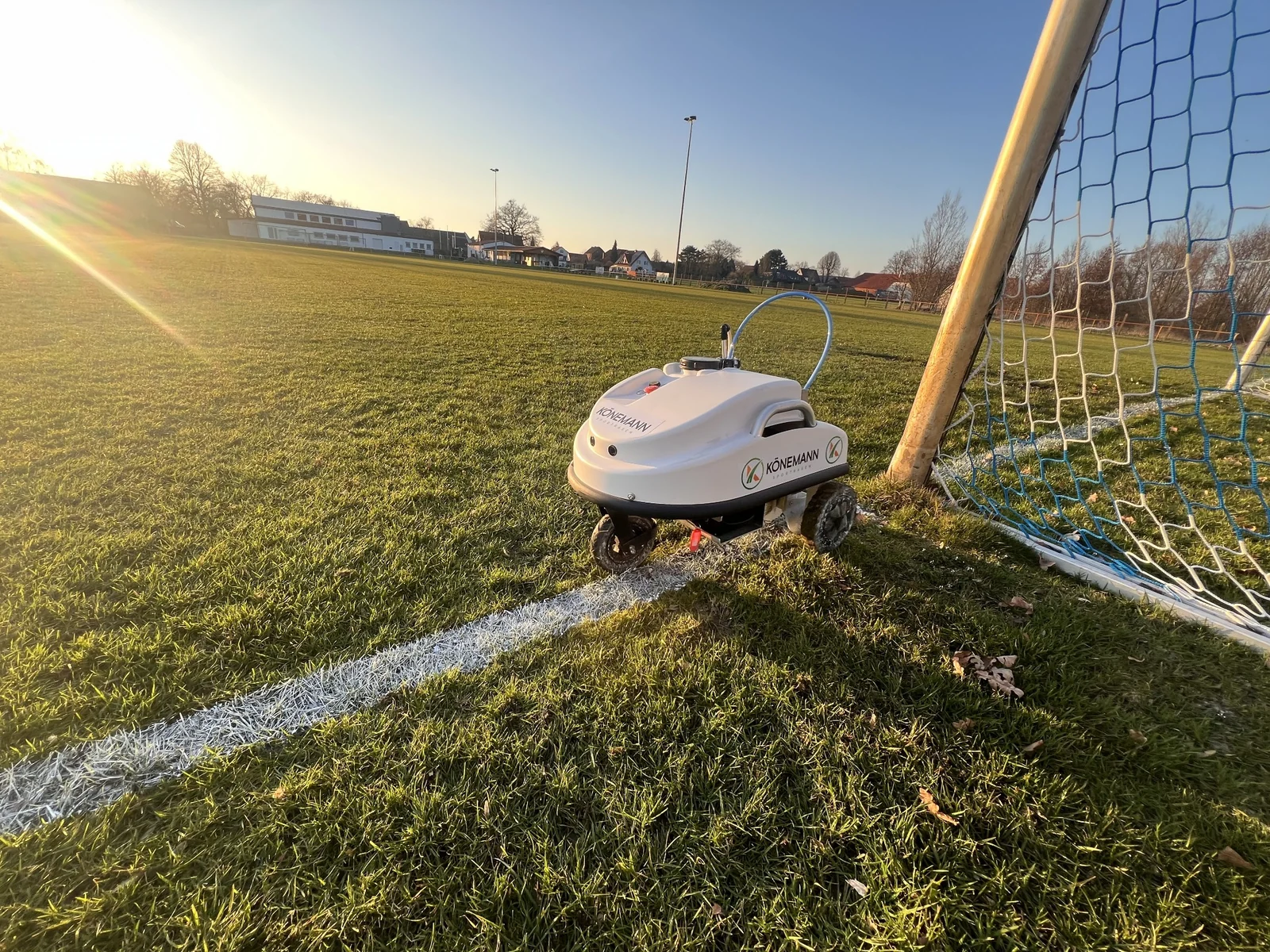 Könemann-Markierroboter am Tor eines Sportplatzes im Abendlicht