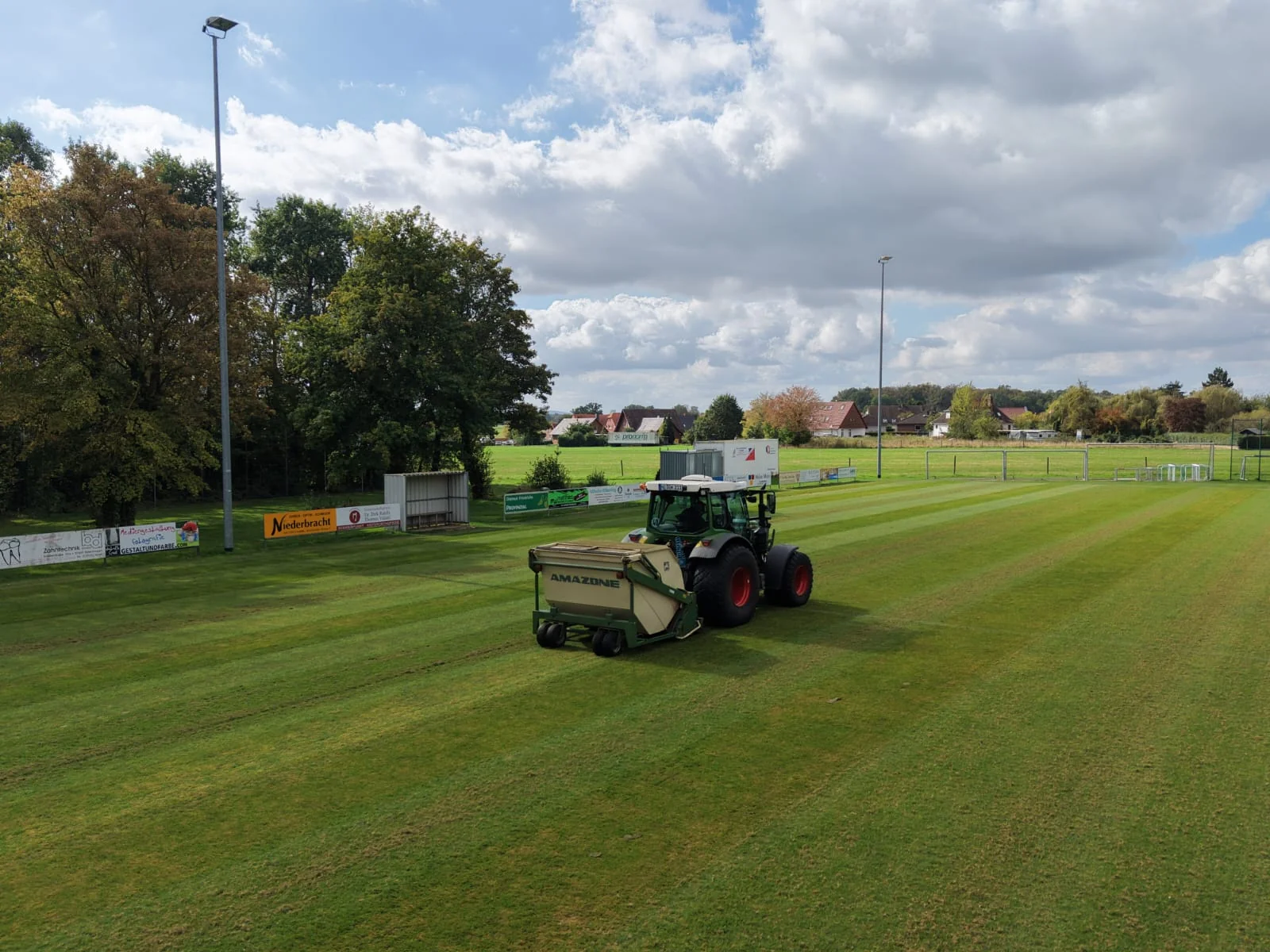 Traktor mit Vertikutier- und Aufnahmetechnik bei der Arbeit auf dem Sportplatz.