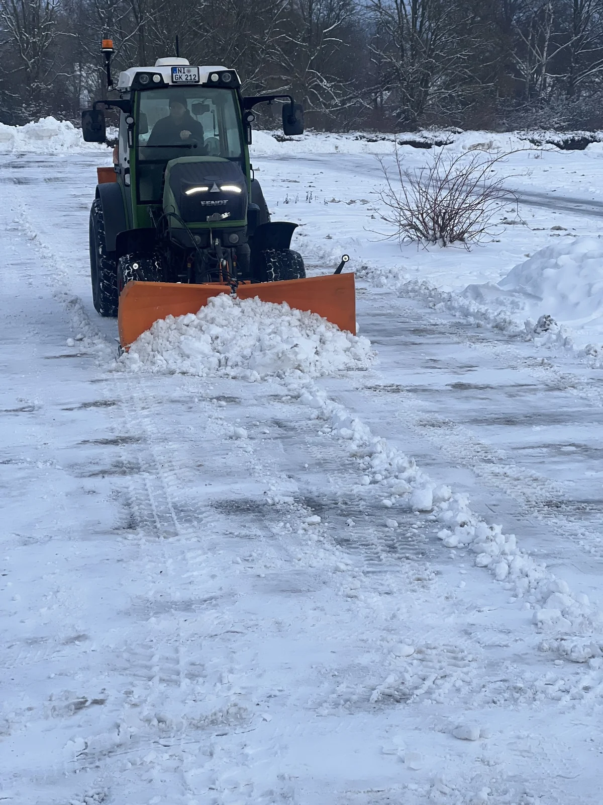 Traktor beim Schneeräumen auf einer verschneiten Verkehrsfläche.
